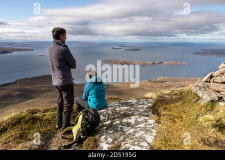 Zwei Wanderer genießen die Aussicht vom Gipfel des Cairn Conmheall über die Sommerinseln, Coigach Peninsula, Wester, Ross, Northwest Highlands of Scotla Stockfoto