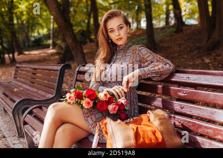 Schöne Frau sitzt auf der Bank mit Strauß Rosen im Herbst Park. Stockfoto