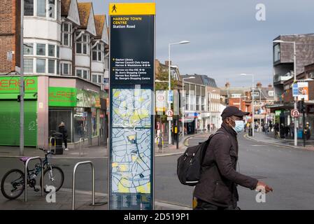 London, Großbritannien. 12. Oktober 2020. Ein Mann mit Gesichtsmask läuft an einem Stadtplan im Stadtzentrum von Harrow vorbei. Es wird berichtet, dass fünf Londoner Stadtbezirke mehr als 100 neue COVID-19 Fälle pro 100,000 Einwohner in der Woche bis zum 8. Oktober hatten - Richmond, Hackney, Ealing, Redbridge und Harrow. Während Großbritannien landesweit einen Anstieg der COVID-19-Fälle erlebt, kündigt Premierminister Boris Johnson im Unterhaus ein neues dreistufiges lokales Sperrsystem an, um die Ausbreitung des Virus zu bekämpfen. Kredit: Stephen Chung / Alamy Live Nachrichten Stockfoto