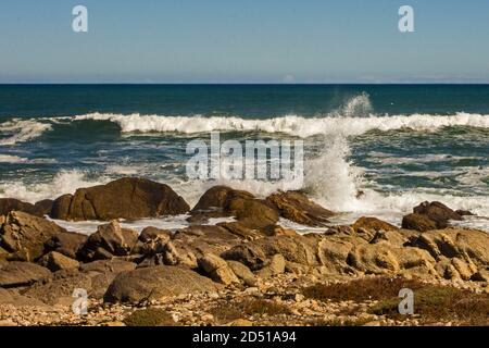 Ein rauschiger Ozean mit Wellen, die spektakulär gegen die Felsbrocken am Ufer des Küstenabschnitts des Namaqua National Park, Südafrika, krachen Stockfoto