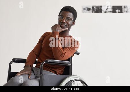 Minimalporträt des jungen afroamerikanischen Mannes mit Rollstuhl und Blick auf die Kamera, während posiert in der modernen Kunstgalerie, kopieren Raum Stockfoto