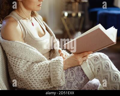 Nahaufnahme der Frau in gestrickter kuscheliger Strickjacke zu Hause im sonnigen Herbsttag Lesebuch. Stockfoto