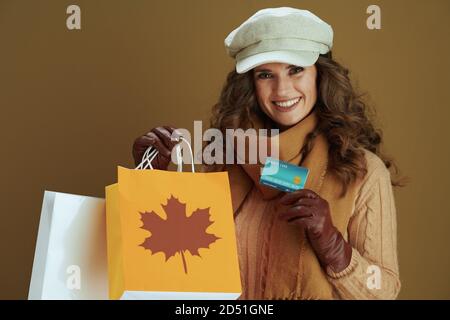 Hallo november. Porträt von glücklich stilvolle mittleren Alters Hausfrau in Pullover mit Lederhandschuhen und Papier Einkaufstasche isoliert auf beige. Stockfoto