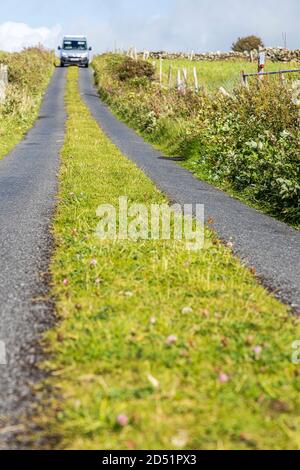 Einspurige Straße mit Gras wächst entlang der Mitte auf der Killeen Schleife Spaziergänge in der Nähe von Louisburgh, County Mayo, Irland Stockfoto