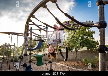 Junges Mädchen hängt kopfüber auf dem Spielplatz Stockfoto