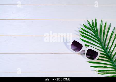 Schöner Sommerurlaub, Sonnenbrillen und Palmenblätter auf weißem Holztisch Stockfoto