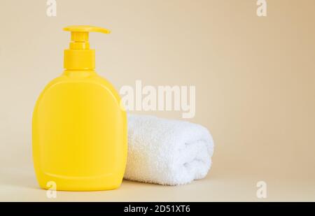 Gelbe Dispenser-Flasche ohne Marke neben weißem Handtuch auf beige Hintergrund Stockfoto