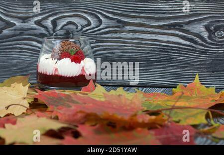 Dessert aus Frischkäse mit Himbeergelee. Dekoriert mit Keksen, Himbeeren und Minze. Getrocknete Herbst Ahornblätter sind überall. Stockfoto