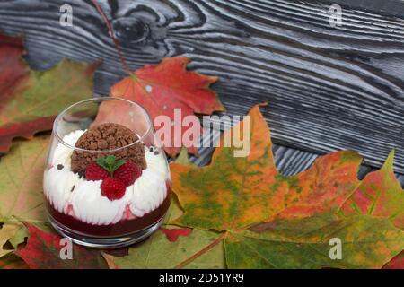 Dessert aus Frischkäse mit Himbeergelee. Dekoriert mit Keksen, Himbeeren und Minze. Getrocknete Herbst Ahornblätter sind überall. Stockfoto