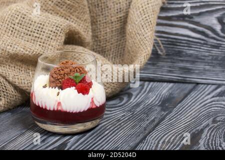 Dessert aus Frischkäse mit Himbeergelee. Dekoriert mit Keksen, Himbeeren und Minze. Auf Kiefernplanken in schwarz. Stockfoto