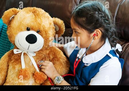 Kleines Mädchen lächelt und spielen Doktor mit brauner Bär und Stethoskop. Kind und Gesundheit Konzept. Stockfoto