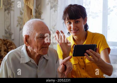 Ein jüngerer Mann und eine junge Frau kommunizieren mit ihren Verwandten über das Telefon. Enkeltochter unterrichtet Großvater online über Smartphone-Apps Stockfoto