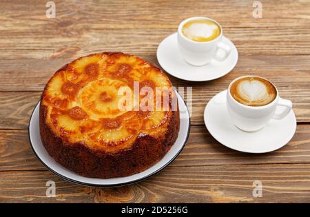 Hausgemachter Ananas-Upside-Down-Kuchen und zwei Tassen Kaffee auf einem Holztisch. Winkelansicht. Stockfoto