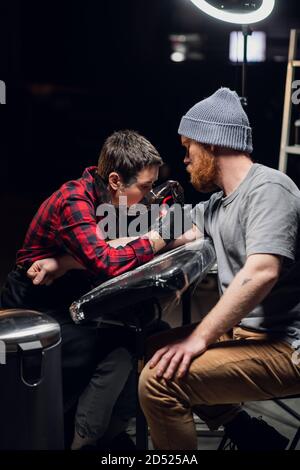 Ein erfahrener Tattoo-Künstler gibt ein Tattoo zu einem weißen skandinavischer Hipster-Mann mit einem roten Bart in seinem Tattoo Salon Stockfoto