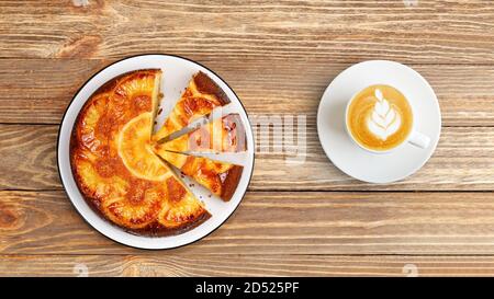 Hausgemachte Ananas Upside Down Kuchen und Tasse Kaffee Cappuccino auf Holztisch. Draufsicht. Stockfoto