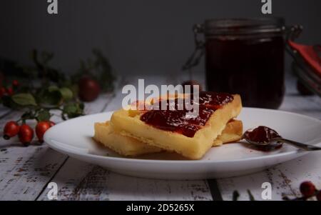 Weiche Waffeln mit Erdbeermarmelade und einem Glas mit Marmelade verschmiert. Stockfoto
