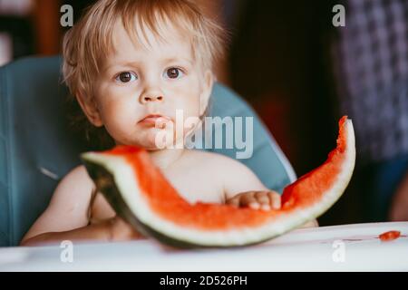 Glücklich Kleinkind Junge essen Wassermelone in seinem Hochstuhl Stockfoto