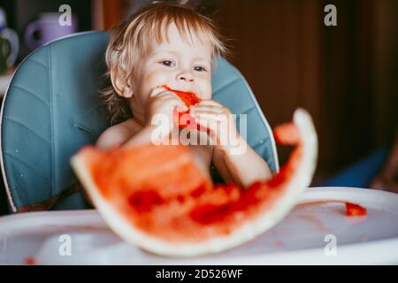 Glücklich Kleinkind Junge essen Wassermelone in seinem Hochstuhl Stockfoto