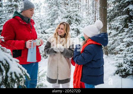 Eine gesunde, freundliche Familie verbringt aktiv ein Wochenende in der Natur, im Winter Fichtenwald bei schönem Schneefall und genießt heißen Tee aus Wanderbechern Stockfoto