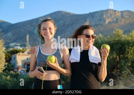 Mutter und Tochter im Teenageralter essen Äpfel nach dem Joggen am Sonnenuntergang Bergstraße Stockfoto