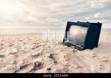 Altes kaputtes Fernsehgerät an einem Strand bei Sonnenuntergang, selektiver Fokus. Stockfoto