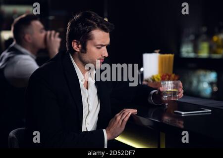 Ein junger Mann trank viel an der Bar und saß betrunken an der Bar mit einem Cocktail. Stockfoto