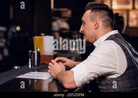 Ein junger Mann in Hemd und Weste bestellt von der Speisekarte an der Bar. Stockfoto