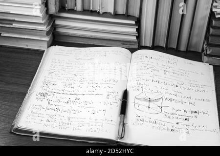 Offenes Schreibbuch mit mathematischen Vorträgen vor dem Hintergrund von Büchern Stockfoto