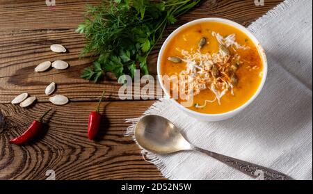 Kürbis-scharfe Sahnesuppe mit Käse und Samen auf einem Holztisch auf einer Tischdecke. In der Nähe ein paar Grüns, rote Paprika, Samen. Stockfoto