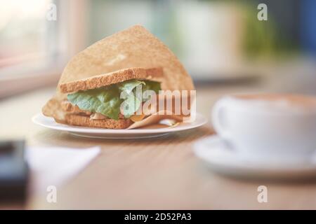 Frisches Frühstück. Tasse Kaffee und Sandwich auf Holztisch im Café, selektiver Fokus Stockfoto