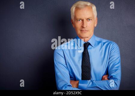 7/8 Schuß von Stattlichen älteren Mann mit Hemd und Krawatte beim Stehen mit verschränkten Armen an dunklen grauen Hintergrund. Stockfoto