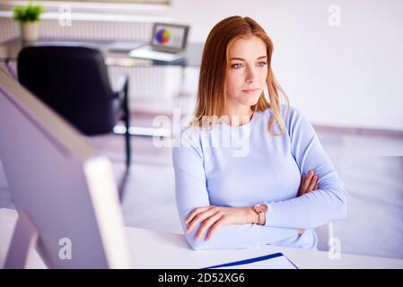 Hohen Winkel shotof attractvie junge geschäftsfrau, Sitzen mit gekreuzten Armen im Büro Schreibtisch und nachdenklich. Stockfoto