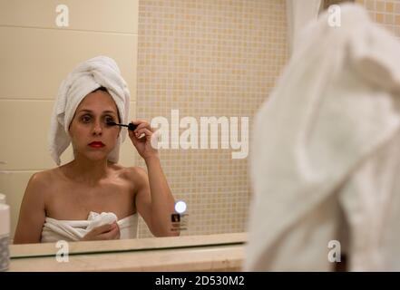 Eine kaukasische Frau im Bademantel und Handtuch auf dem Kopf Make-up nach einem Bad Stockfoto
