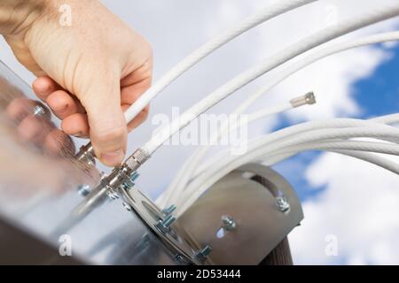 Man's Hand Verbindungskabel zu 4G-Antenne Nahaufnahme mit Himmel auf Hintergrund. Stockfoto