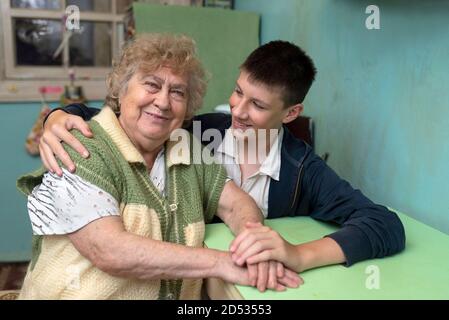 Teenager Enkel umarmt seine Großmutter in der Küche zu Hause. Arme, echte Menschen. Stockfoto