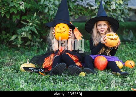 Frohe Halloween. Zwei lustige Kinder in Hexenanzügen und mit Kürbissen sitzen draußen Stockfoto