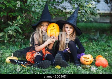 Frohe Halloween. Zwei lustige Kinder in Hexenanzügen und mit Kürbissen sitzen draußen Stockfoto