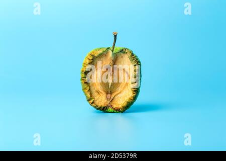 Alter getrockneter Apfel auf blauem minimalem Hintergrund. Verdorbenes und geschrumpftes Obst und Gemüse. Alter und Hautkonzept. Stockfoto