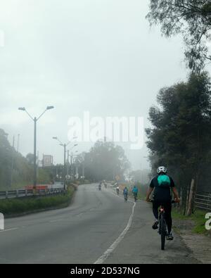 Vertikale Aufnahme von Bikern Fahrrad fahren auf der Seite der Die Straße an einem nebligen Tag Stockfoto