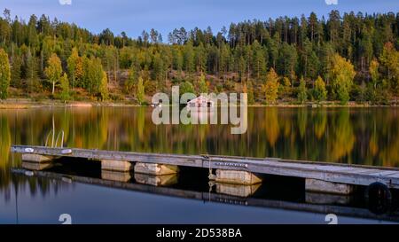 Steg im Vordergrund und ein rotes Bootshaus und Wald Im Herbst Farben im Hintergrund Stockfoto