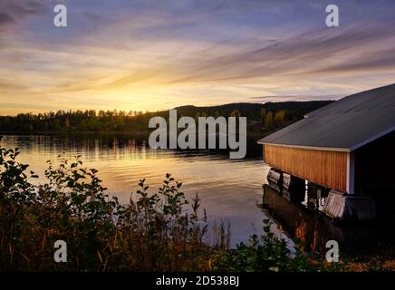 Ein rotes Bootshaus am Meer mit Sonnenuntergang im Hintergrund Stockfoto