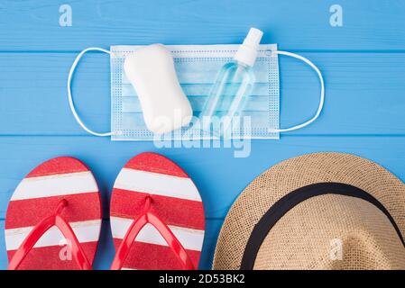 Urlaubs- und Quarantänekonzept. Oben über Overhead-Ansicht Foto von Seife Desinfektionsmittel Maske Flipflops und Hut isoliert auf blauem Hintergrund Stockfoto