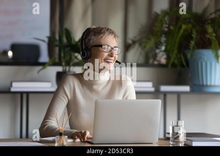 Lächelnde Mitarbeiterin in Kopfhörern lacht beim Videoanruf Stockfoto
