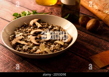 Pilzrisotto, italienische Küche, auch Risotto ai funghi genannt, Blick von oben mit warmem Licht, Petersilie, Seitenansicht, auf dunkelbraunem Holztisch. parmesan-Flocken Stockfoto