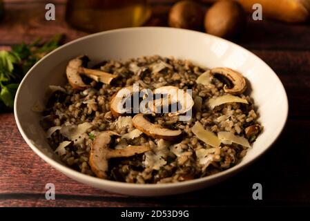 Risotto mit Pilzen, italienische Küche, bekannt als Risotto ai funghi, Nahaufnahme mit warmem Licht, Petersilie, Seitenansicht, auf dunkelbraunem Holztisch. parmesan-Flocken Stockfoto