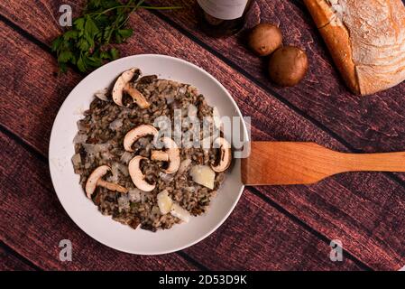 Champignon-Pilz-Risotto, italienische Küche als 'Risotto ai funghi' bekannt, Ansicht von oben mit warmem Licht, Petersilie, Seitenansicht, auf dunkelbraunem Holztisch. Parm Stockfoto