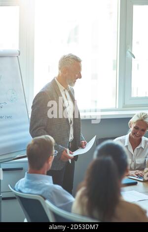 Vertikale Aufnahme eines selbstbewussten reifen Geschäftsmann halten Dokument und Lächelnd, während wir mit den Collegaues über ein neues Projekt sprechen Stockfoto