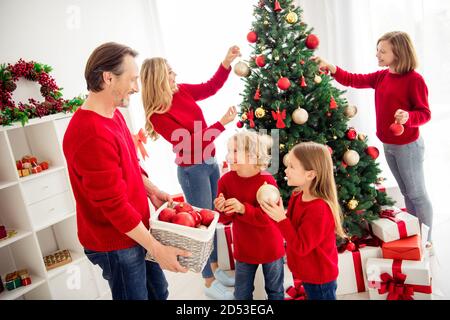 Foto der ganzen großen Familie fünf Leute treffen drei kleine Kinder schmücken Weihnachtsbaum Papa helfen Sohn Tochter halten Ball Tragen Sie roten Pullover Jeans zu Hause Stockfoto