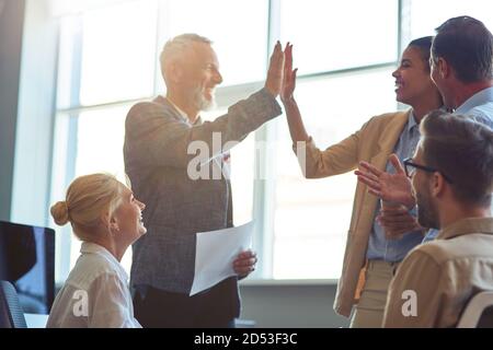 Erfolg wird gefeiert. Glücklich reifen Mann und junge Frau geben hohe fünf aufeinander nach dem Treffen mit Kollegen, die Arbeit in der modernen Büro oder Stockfoto