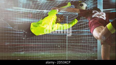 Fußball-Torwart, in fluoreszierender Uniform, macht einen Save auf einen nahen Kopfschuss des Angreifers Stockfoto